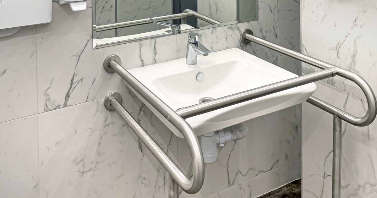 Salle de bain adaptée avec douche à l'italienne, barres d'appui inox et tapis antidérapant.